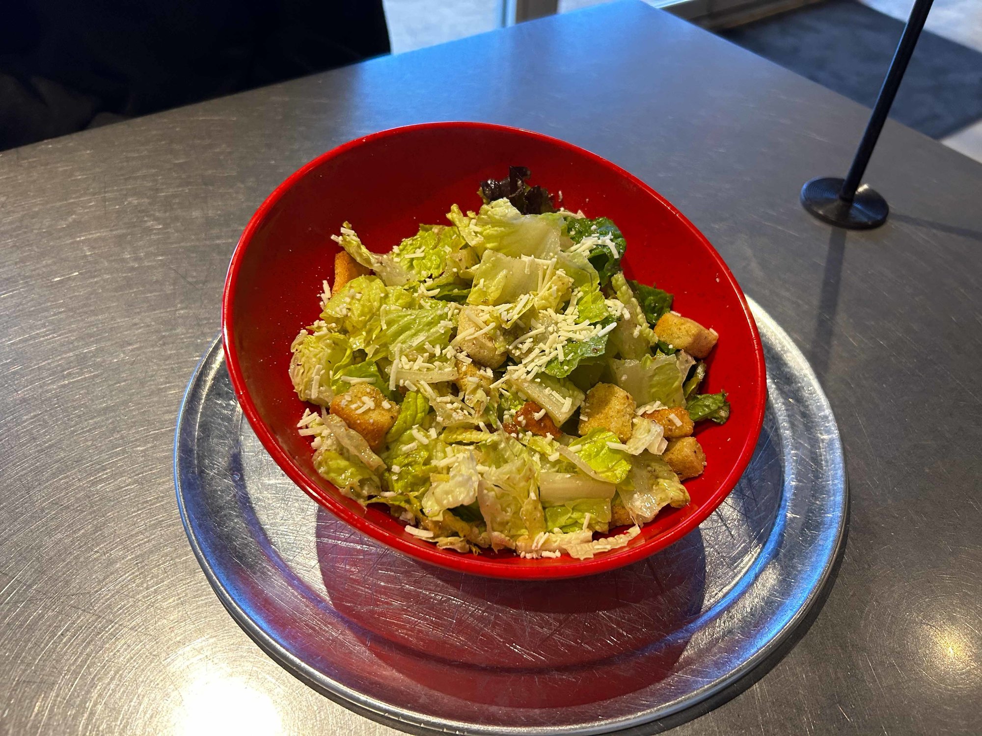 caesar salad in a red bowl on a metal table